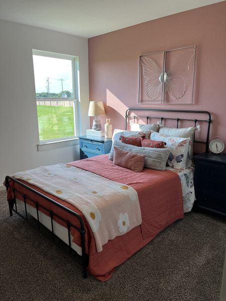 A cozy bedroom with a pink accent wall, butterfly art, and charming decor in soft, warm tones.