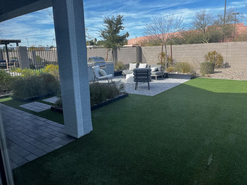 Spacious backyard with artificial grass, a built-in barbecue, and a stylish outdoor seating area.