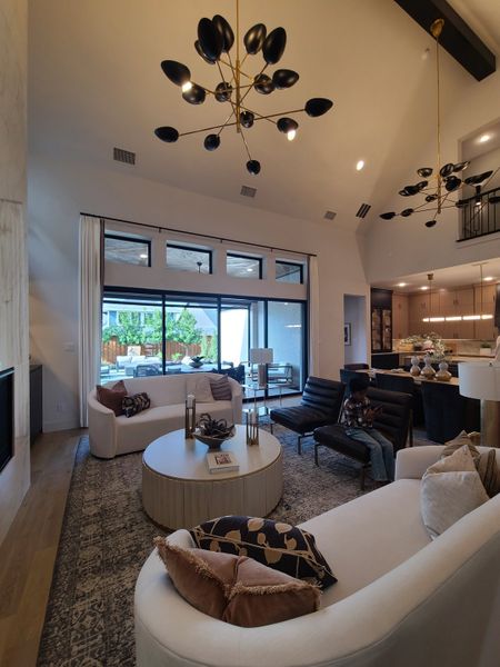 A chic living room featuring elegant chandeliers, plush seating, and a large window overlooking the patio.