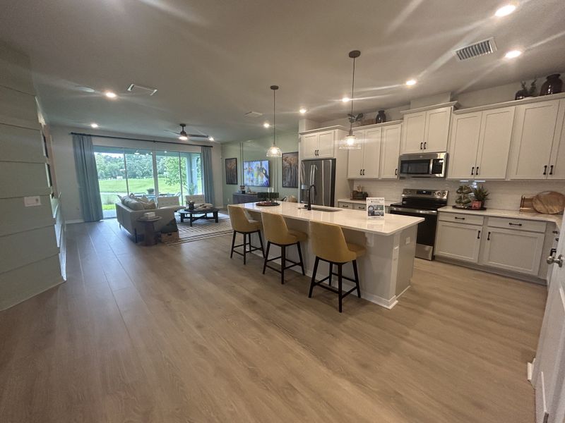 Spacious open-concept kitchen and living area with sleek cabinetry, large island, and scenic backyard views.