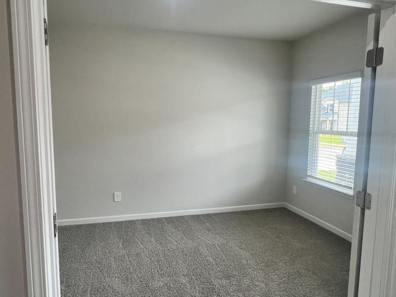 A bright, carpeted room with soft gray walls and large window flooding light, creating a cozy, inviting space. A bright, carpeted room with soft gray walls and large window flooding light, creating a cozy, inviting space.