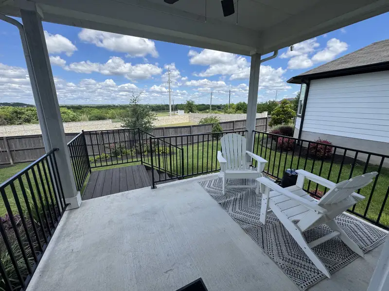 A cozy porch with white chairs, a patterned rug, and a lovely backyard view under a blue sky.