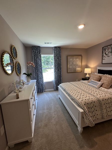 A cozy bedroom with a white dresser, patterned curtains, elegant mirrors, and plush bedding.