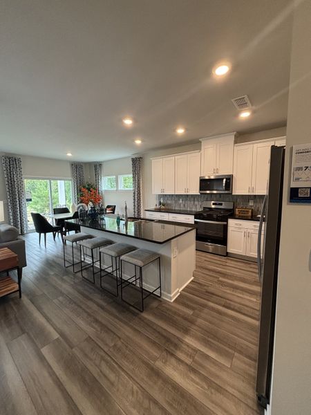 A modern kitchen with dark wood floors, white cabinets, a sleek island, and ample natural light.