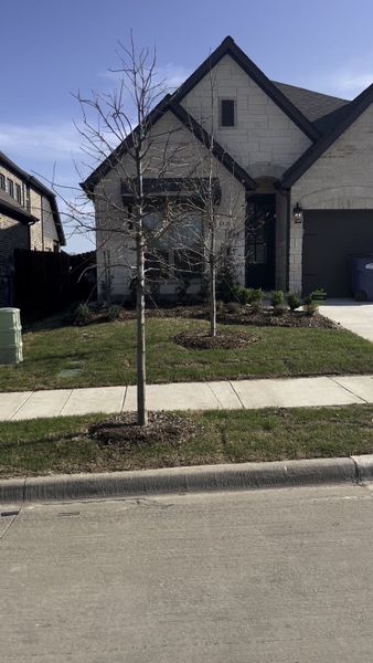 A charming stone facade with a manicured lawn in Woodland Creek by UnionMain Homes (Royse City, TX).