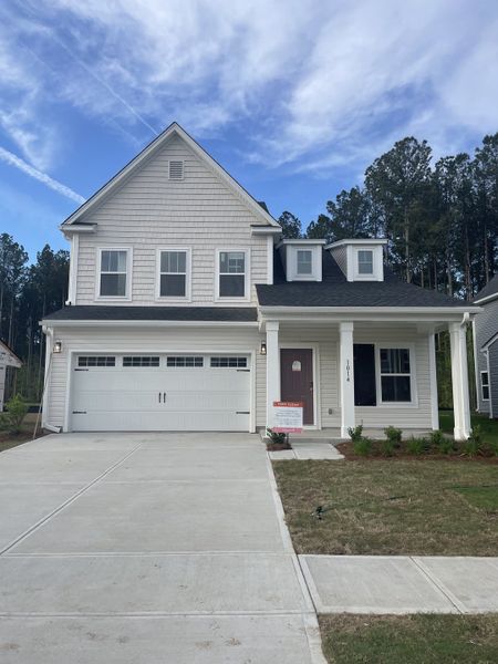 A charming white home with a spacious garage and inviting porch in Homecoming by True Homes (Ravenel, SC).
