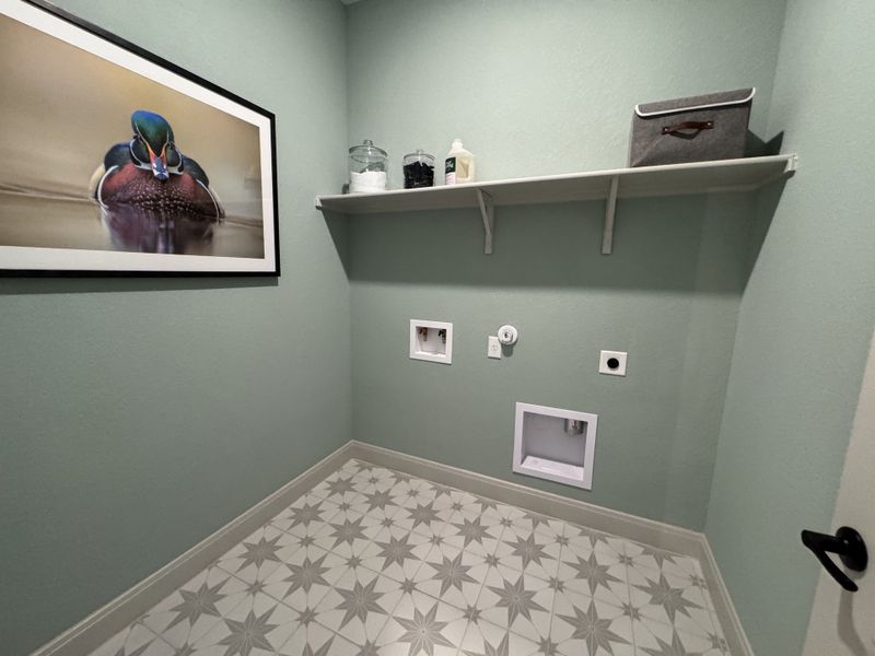 A charming laundry room with patterned tile flooring, mint green walls, and a sleek floating shelf for storage.