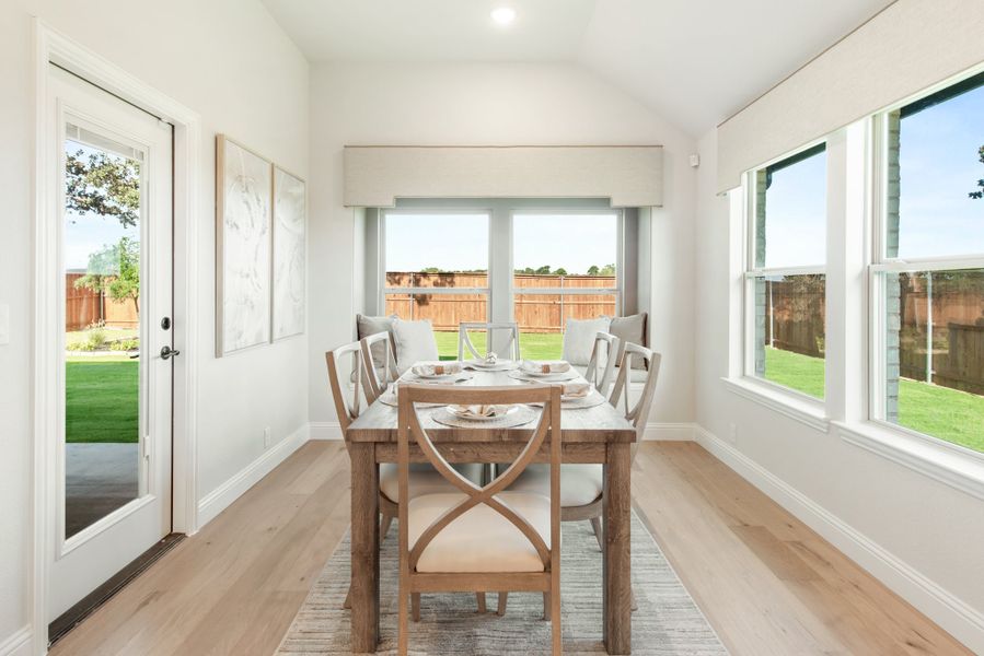 Bright dining area with wood table, four chairs, vaulted ceiling, and large windows overlooking a backyard. Bright dining area with wood table, four chairs, vaulted ceiling, and large windows overlooking a backyard.