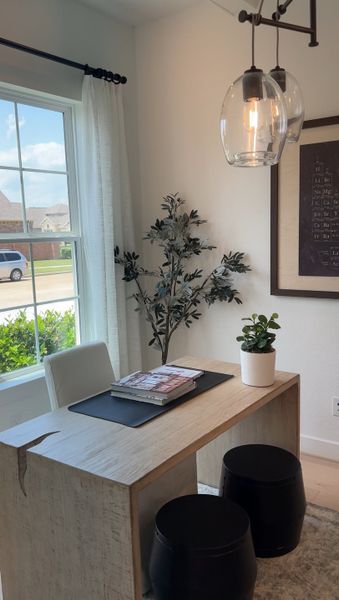 A chic home office with a sleek wooden desk, modern pendant lights, and lush greenery for a serene work environment.