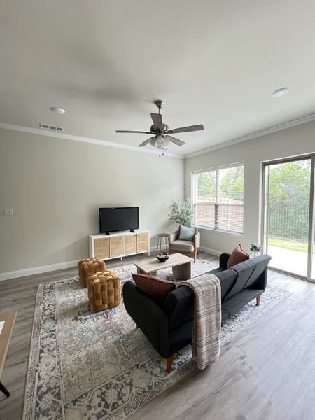 A cozy living room with a patterned rug, sleek black sofa, and natural light from large windows.