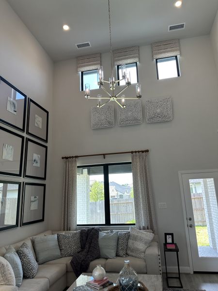 A modern living room with high ceilings, chic chandelier, and cozy sectional seating beneath elegant artwork and tall windows. A modern living room with high ceilings, chic chandelier, and cozy sectional seating beneath elegant artwork and tall windows.