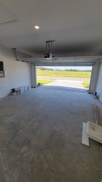 A spacious, well-lit garage with a concrete floor and open door leading to a paved driveway.