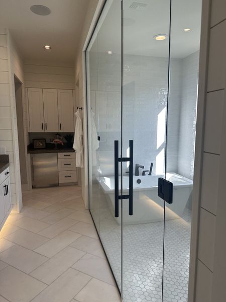 A sleek bathroom featuring a glass-enclosed tiled shower, soaking tub, and modern cabinetry.