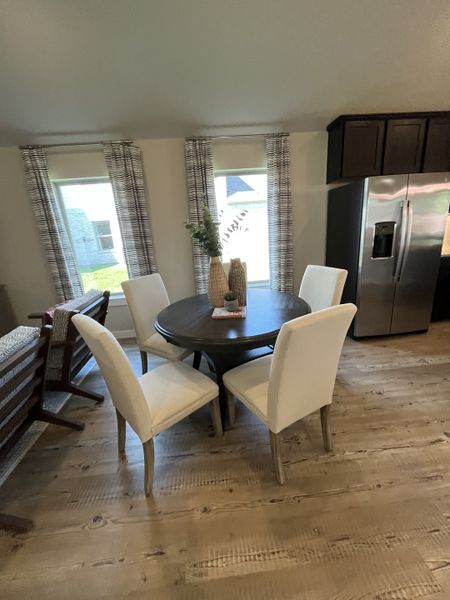 A cozy dining area with a round table, white upholstered chairs, and natural wood flooring.