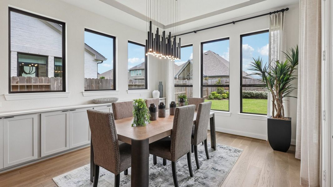 Sunlit dining space with chic chandelier and expansive windows in Brookewater. Luxurious hardwood floors enhance elegance.