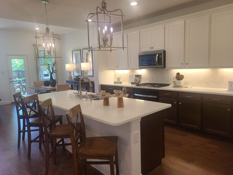 A modern kitchen with white cabinetry, an island with seating, pendant lighting, and wood floors. Bright and inviting space.