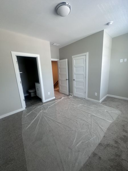 A cozy bedroom with neutral walls, plush carpet, and an adjoining bathroom, creating a serene and inviting atmosphere.