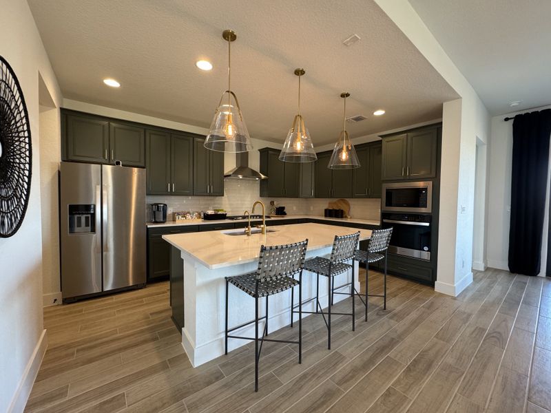 A modern kitchen featuring dark cabinets, stainless steel appliances, and elegant pendant lighting over a large island.