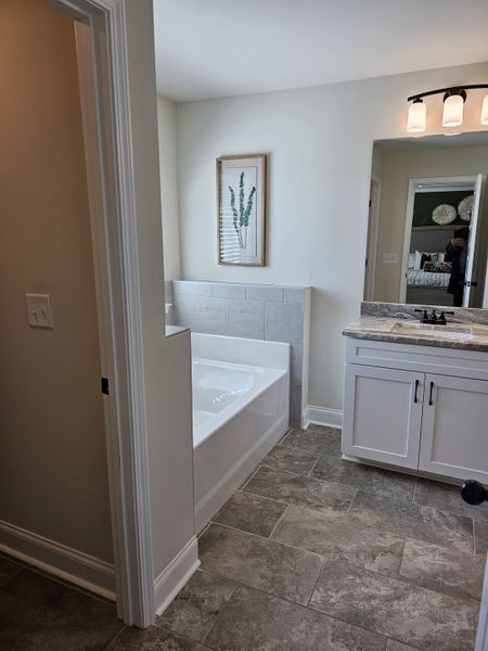 A modern bathroom features a sleek tub, gray tile flooring, and a bright vanity with stylish lighting.