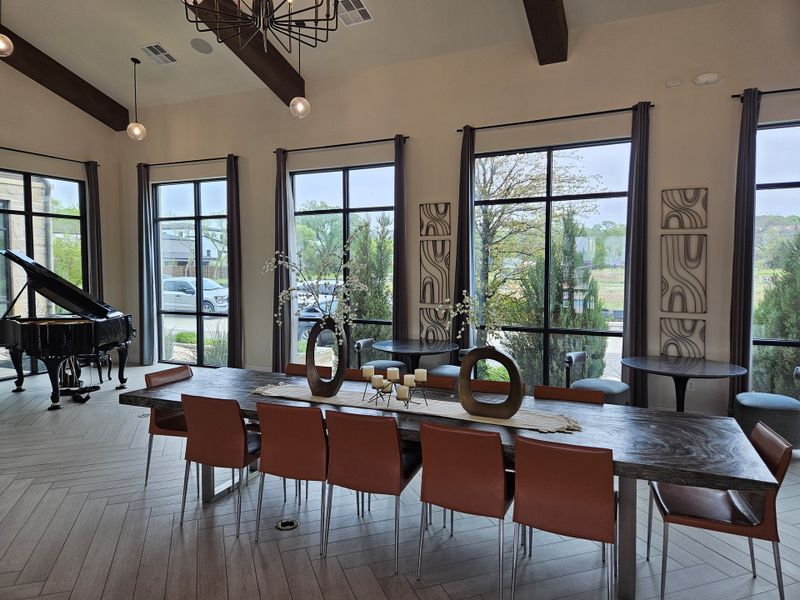 A chic dining area with large windows, a grand piano, elegant decor, and modern leather chairs.