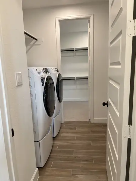 A sleek laundry room with modern appliances, wood-look tile flooring, and open shelving.