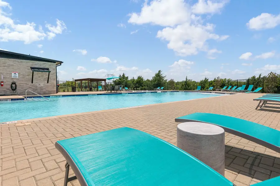 Community swimming pool with brick patio, teal lounge chairs, and a pergola seating area
