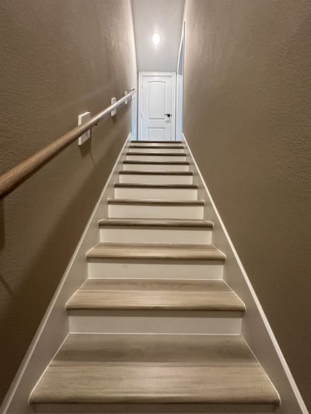 A contemporary staircase with neutral walls and wood steps, leading to a sleek white door with soft lighting. A contemporary staircase with neutral walls and wood steps, leading to a sleek white door with soft lighting.