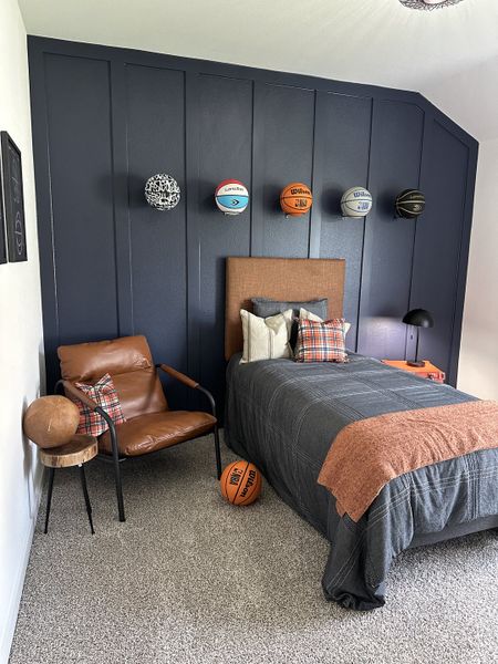 A cozy bedroom featuring a modern leather chair, sports-themed decor, and a dark accent wall with basketball displays. A cozy bedroom featuring a modern leather chair, sports-themed decor, and a dark accent wall with basketball displays.