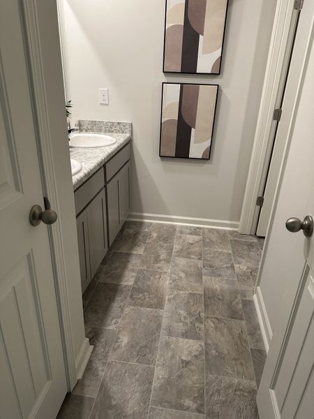 A modern bathroom featuring dual sinks, abstract wall art, and gray tiled flooring.