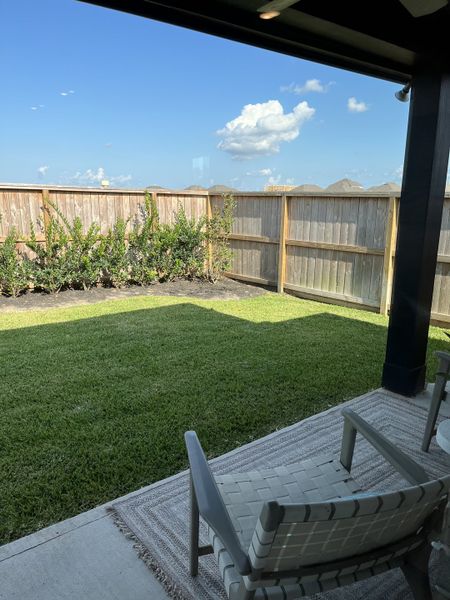A serene backyard patio with woven chairs overlooking a lush green lawn and wooden fence under a clear blue sky. A serene backyard patio with woven chairs overlooking a lush green lawn and wooden fence under a clear blue sky.