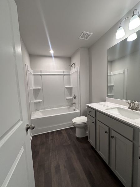 A modern bathroom with a sleek bathtub, elegant vanity, and tasteful lighting on dark wood flooring.