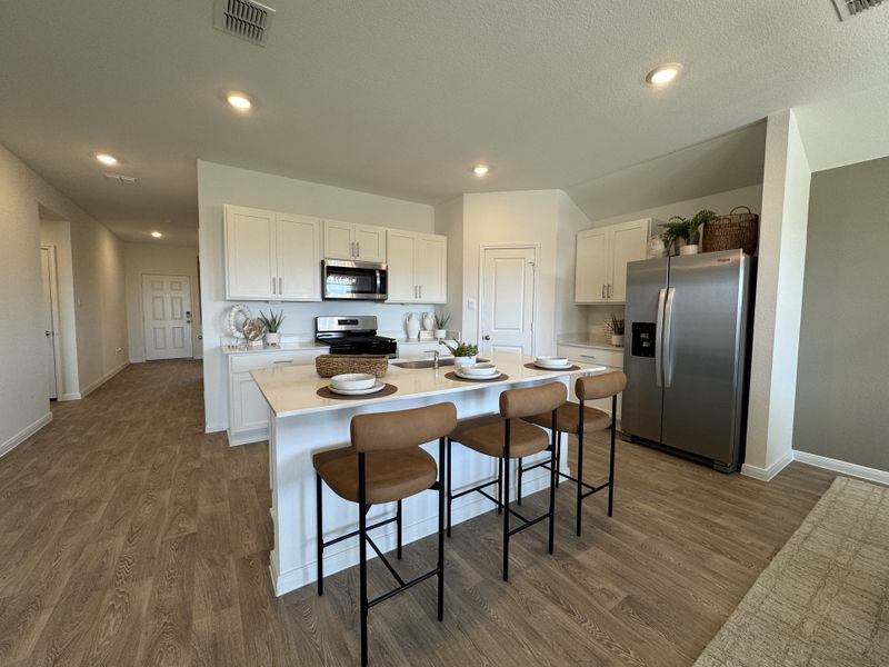 A modern kitchen with a large island, stainless steel appliances, wood floors, and sleek white cabinetry. A modern kitchen with a large island, stainless steel appliances, wood floors, and sleek white cabinetry.