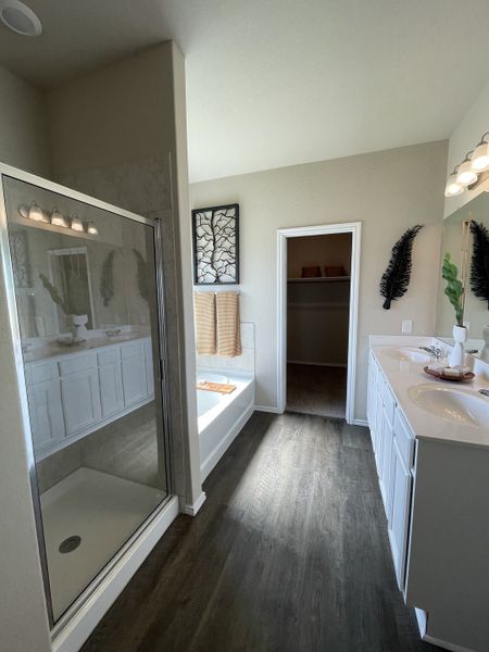 A modern bathroom with elegant flooring, dual sinks, a glass shower, and a cozy tub area for relaxation.