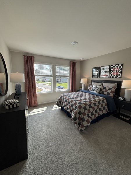 A cozy bedroom featuring a checkered bedspread, racing-themed decor, and ample natural light from large windows.