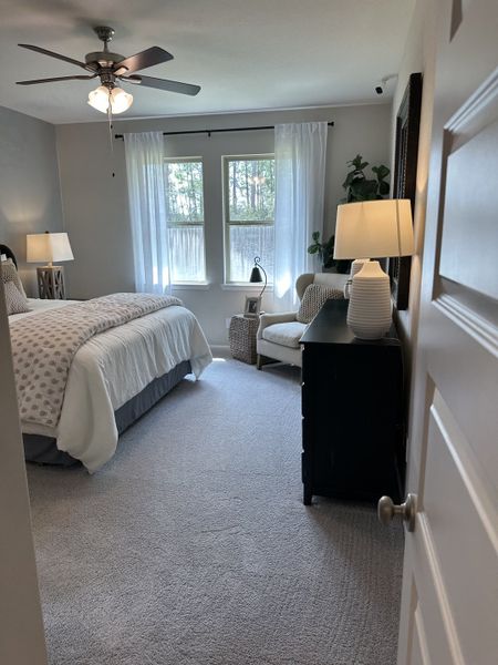 A cozy bedroom with soft carpeting, elegant bedding, and ample natural light through large windows, creating a serene retreat.