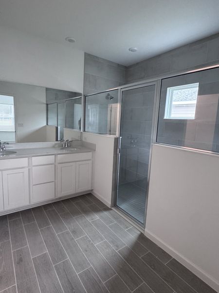 A modern bathroom with sleek gray tiles, a double vanity, and a spacious glass shower.