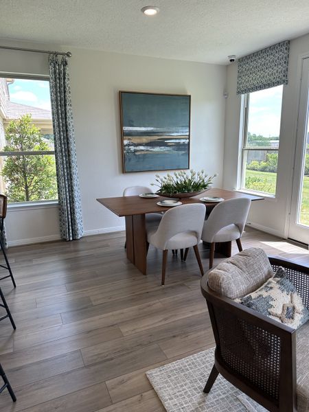 A bright dining area with modern decor, wooden floor, and large windows showcasing garden views.