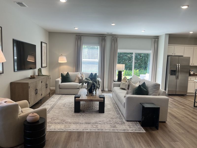 A modern living room with chic sofas, mounted TV, elegant decor, and large windows overlooking greenery.