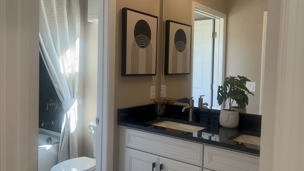 A modern bathroom with dual sinks, black countertops, abstract art, and natural light streaming through a window. A modern bathroom with dual sinks, black countertops, abstract art, and natural light streaming through a window.
