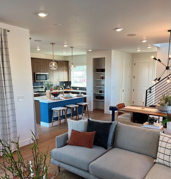 A modern open-concept living area with a gray sofa, sleek kitchen island, and stylish dining space, enhanced by chic lighting.