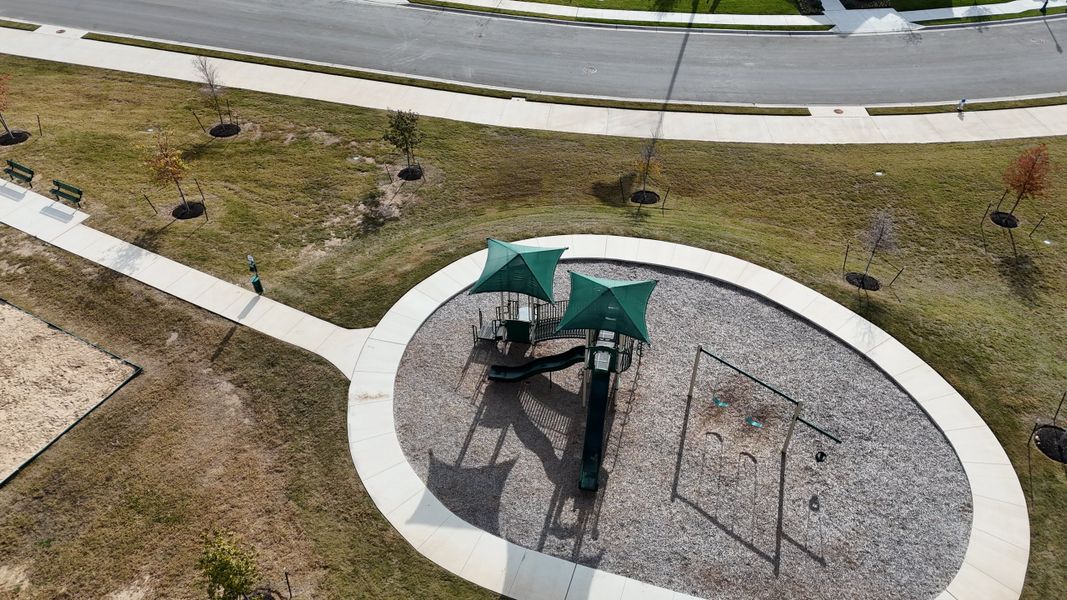 A vibrant green playground with slides and swings, offering fun for kids in Riverview by Brightland Homes (Georgetown, TX).

