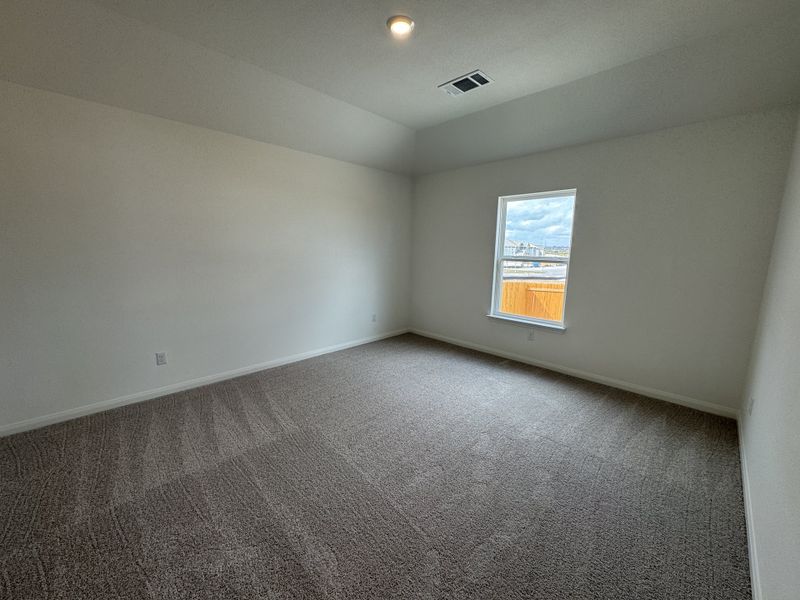 A spacious bedroom with neutral walls, plush carpet, and a large window bringing in natural light.