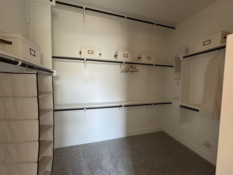 A spacious walk-in closet with ample shelving, hanging rods, and carpeted flooring for organized storage.