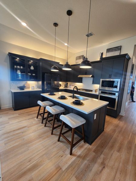 A chic kitchen featuring dark cabinetry, sleek countertops, and modern pendant lighting with light wood flooring. A chic kitchen featuring dark cabinetry, sleek countertops, and modern pendant lighting with light wood flooring.