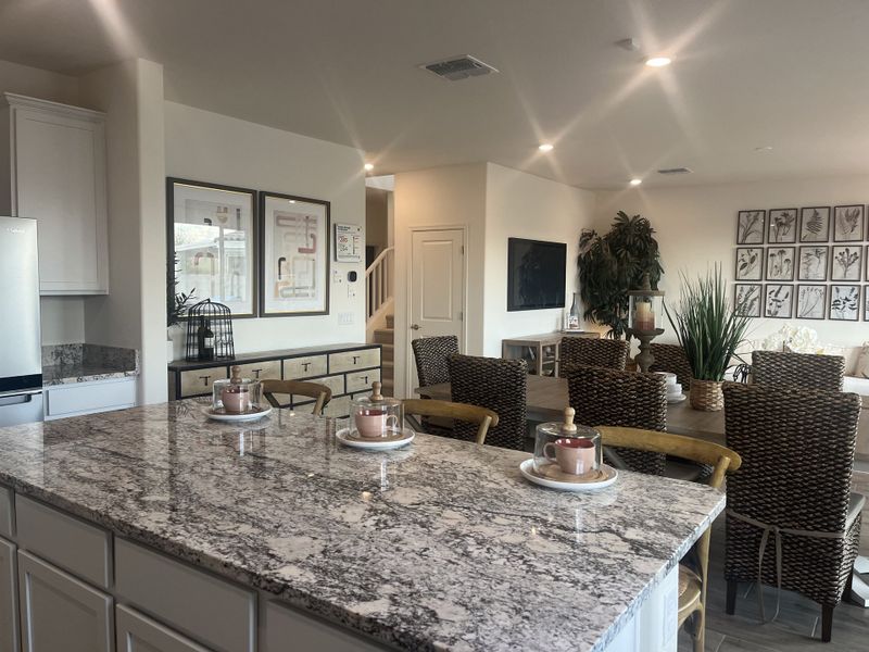 A modern kitchen and dining area with a granite island, wicker chairs, and elegant decor.