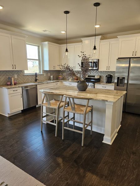A modern kitchen with white cabinets, a stylish island, dark wood floors, and elegant pendant lighting.