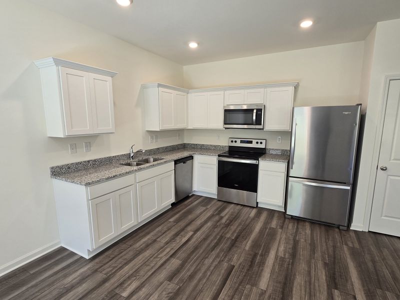 A modern kitchen featuring white cabinets, granite countertops, stainless steel appliances, and wood-look flooring.