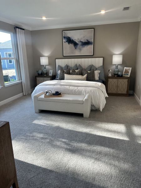 A serene bedroom with soft gray tones, plush carpeting, elegant lamps, and abstract artwork above the inviting bed.