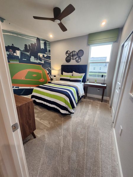 A vibrant bedroom with a sports-themed mural, striped bedding, and a stylish ceiling fan. Perfect for a young sports enthusiast.