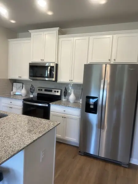 A modern kitchen featuring granite countertops, white cabinets, stainless steel appliances, and a sleek wood floor. A modern kitchen featuring granite countertops, white cabinets, stainless steel appliances, and a sleek wood floor.